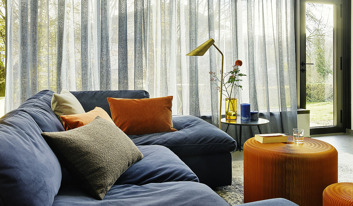 Wohnzimmer mit gemütlicher Couch und großem leicht transparenten Vorhang